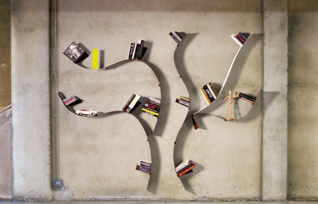 Libreria da parete simile ad un albero con mensole in acciaio flessibile.